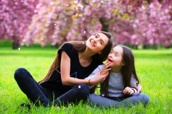Woman Sitting in the Grass with a Happy Girl — Disability Services in Toowoomba, QLD