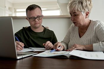 Caucasian Adult Man With Down Syndrome Studying With His Mum At Home — Disability Services & Support in Ipswich, QLD