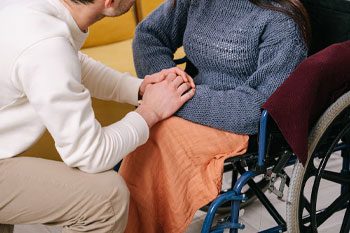 Man Holding Woman's Hand Sitting On A Wheelchair — Disability Services & Support in Sunshine Coast, QLD