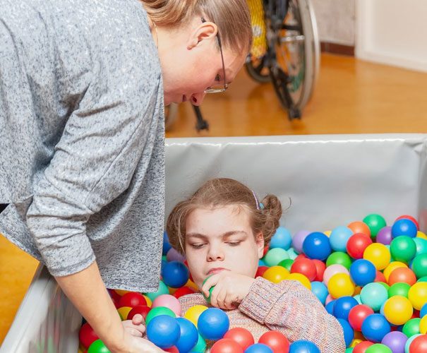 Nurse Helping A Child Play Inside A Ballpit