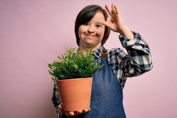 Young Girl With Down Syndrome Holding A Pot With Green Plant