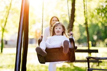 A Child Enjoying the Swing Outdoors With Sister — Disability Services in Bundaberg Central, QLD